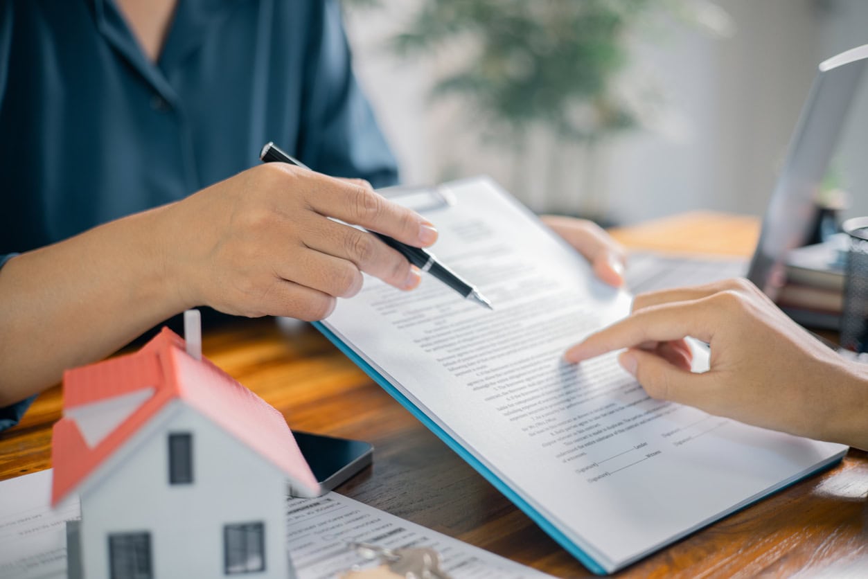 Person reviewing and signing a home-related document with a real estate agent, with a small house model on the table, representing homeowner resources